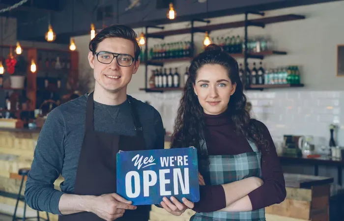 Two cafe owners with a Yes We’re Open sign, highlighting local businesses customers can discover in the directory